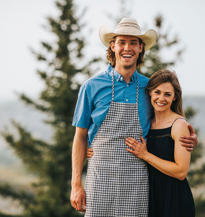 A cowboy and his wife stand in in front of a spruce tree